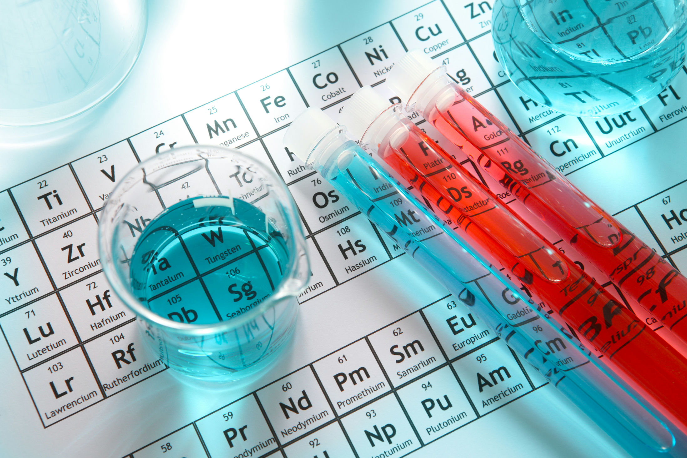 Foto di un becker pieno di liquido blu e di una provetta con liquido rosso sopra una tavola periodica degli elementi