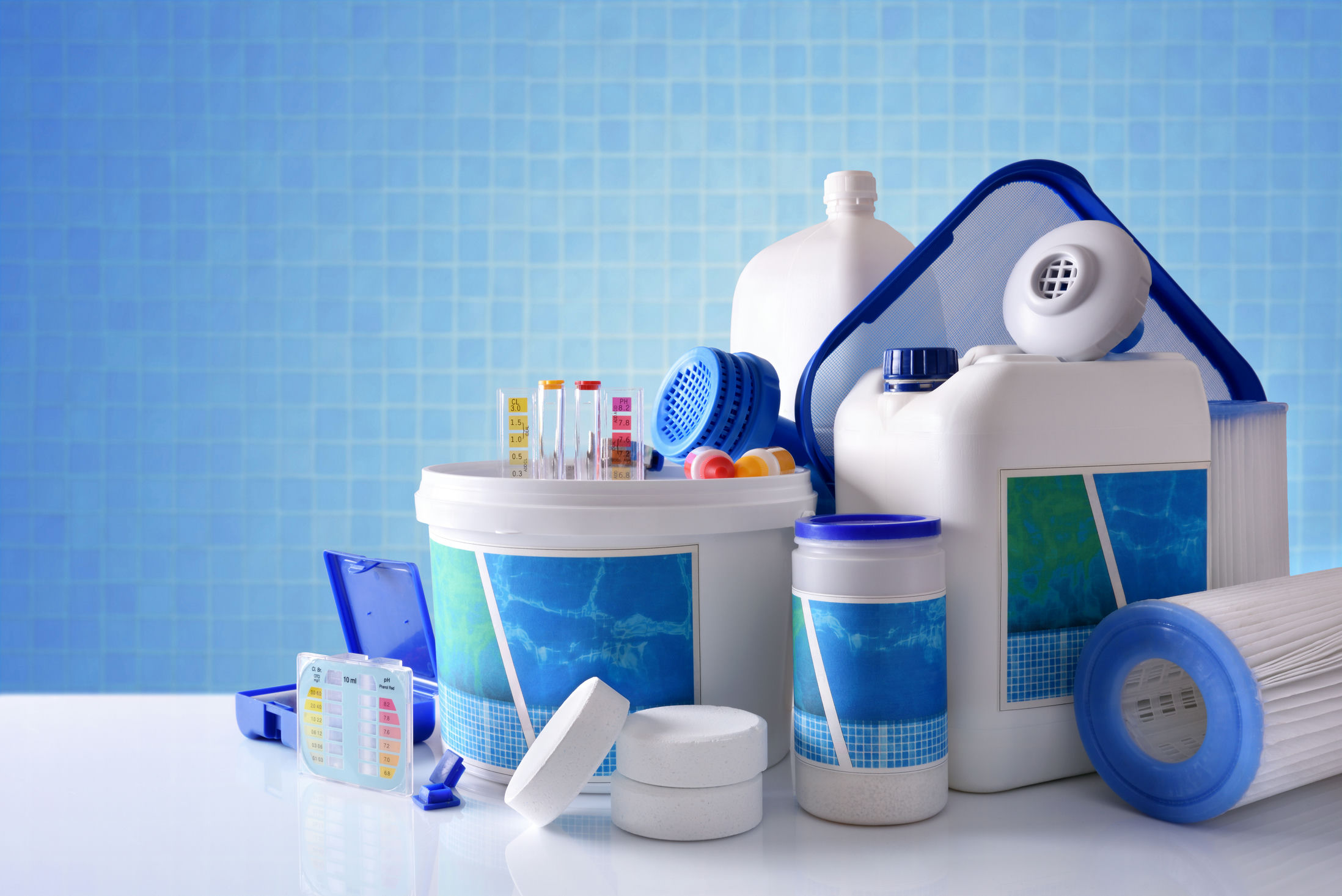 Chemical cleaning products for pool water on white table and blue mosaic background. Horizontal composition. Front view
